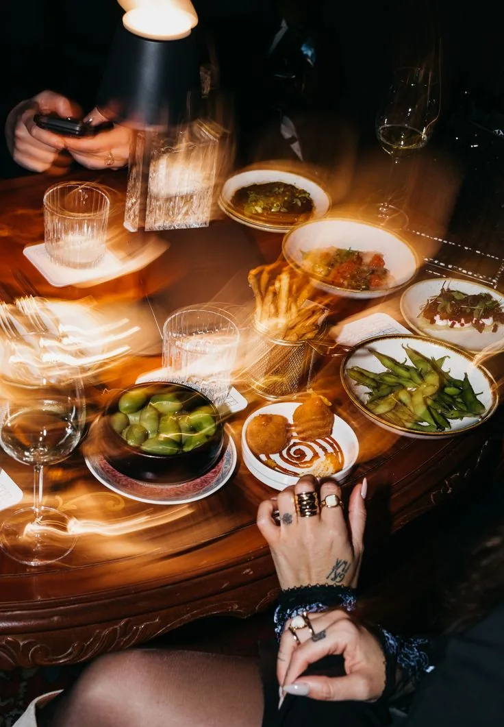 Shared plates and glassware on a candlelit table among friends