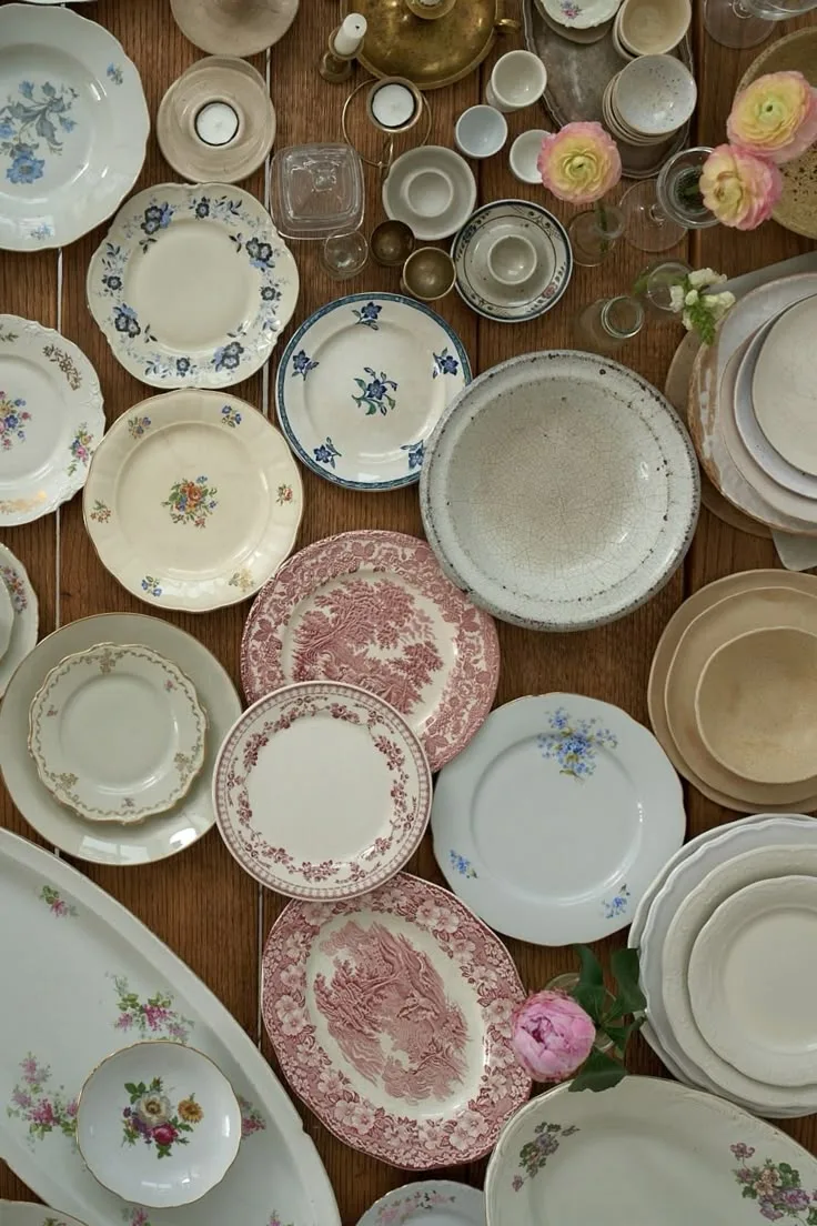 Collection of vintage floral porcelain plates and glassware laid across a wooden table